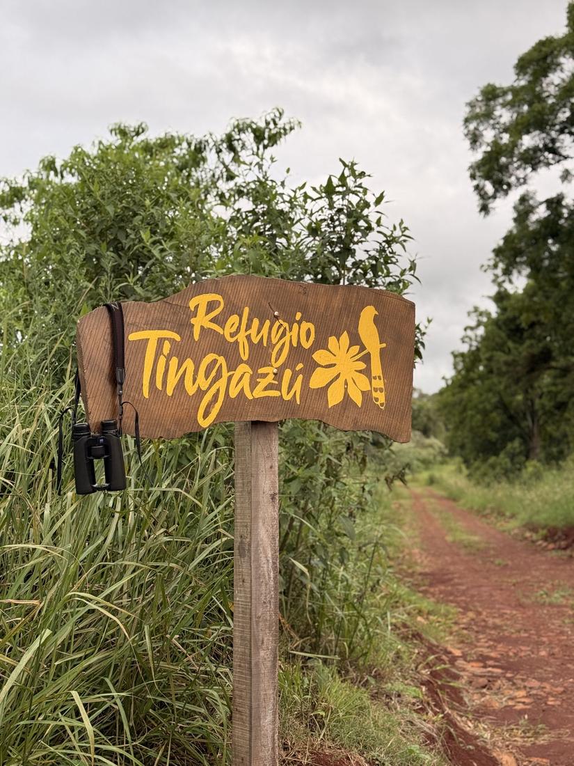 Cartel de Refugio Tingazú en la entrada, junto al camino de tierra colorada